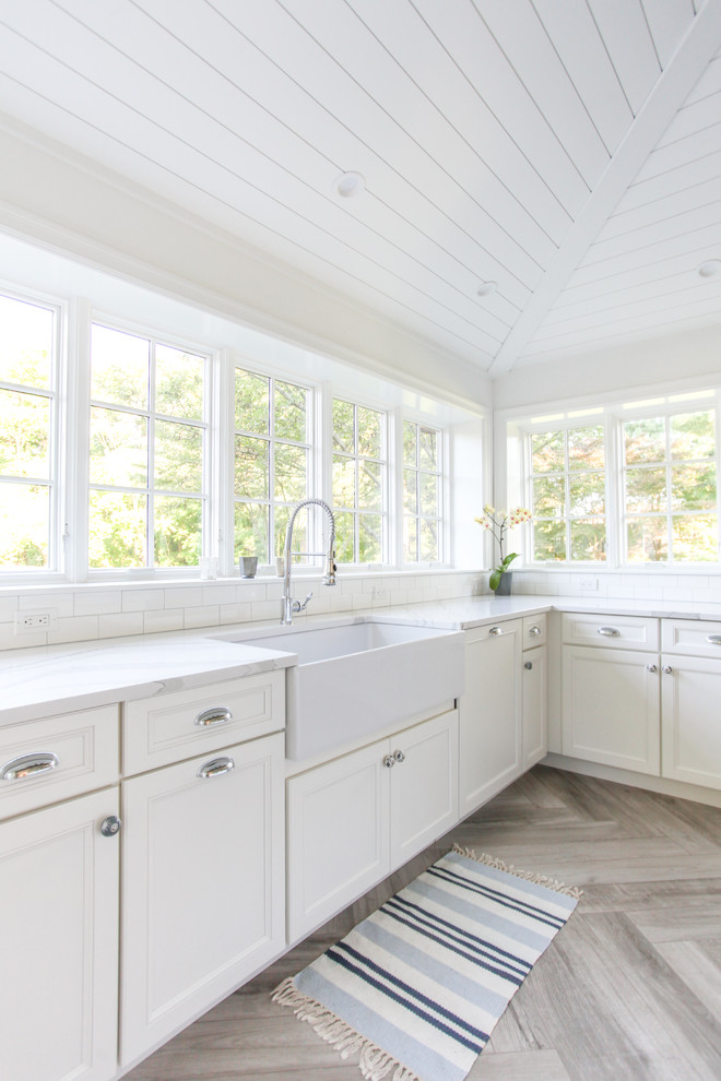 Inspiration for a large beach style u-shaped eat-in kitchen in New York with a farmhouse sink, shaker cabinets, white cabinets, quartz benchtops, white splashback, subway tile splashback, panelled appliances, porcelain floors, with island, grey floor and white benchtop.