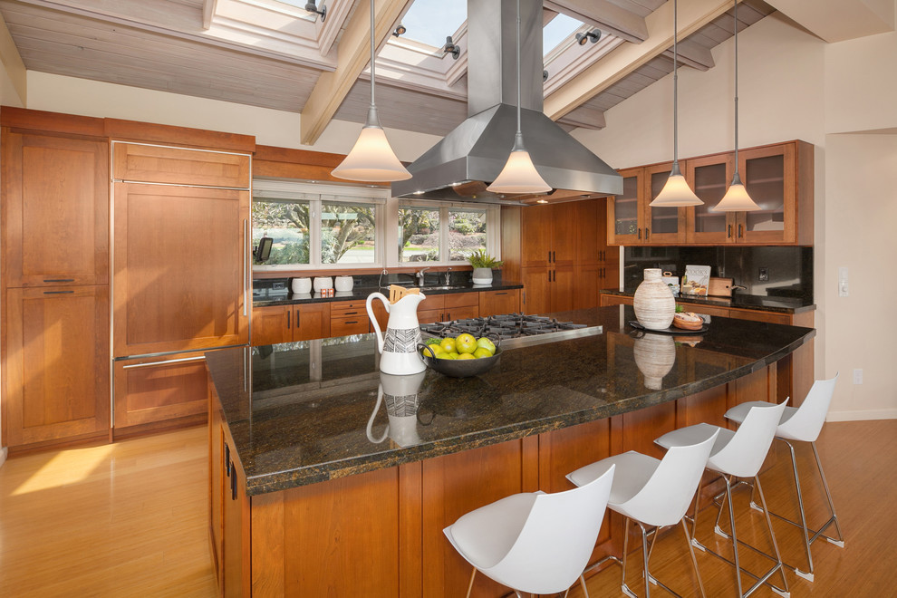 This is an example of a midcentury kitchen in Seattle with an undermount sink, shaker cabinets, medium wood cabinets, panelled appliances, medium hardwood floors, with island and black benchtop.