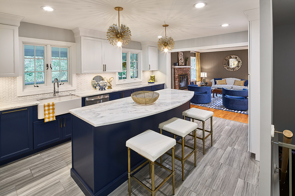 Photo of a mid-sized transitional l-shaped eat-in kitchen in Charlotte with a farmhouse sink, recessed-panel cabinets, blue cabinets, marble benchtops, white splashback, mosaic tile splashback, stainless steel appliances, porcelain floors, with island, grey floor and white benchtop.