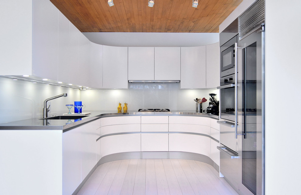 Small trendy u-shaped bamboo floor enclosed kitchen photo in DC Metro with an integrated sink, flat-panel cabinets, white cabinets, stainless steel countertops, glass sheet backsplash, stainless steel appliances and white backsplash