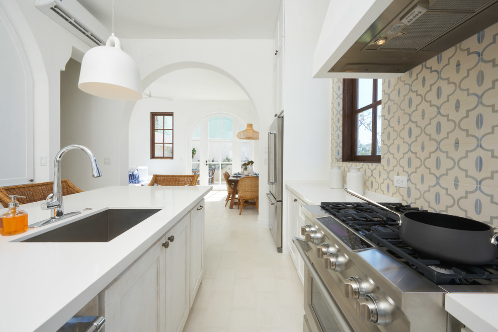 Design ideas for a mid-sized beach style galley eat-in kitchen in Other with an undermount sink, shaker cabinets, white cabinets, quartz benchtops, multi-coloured splashback, cement tile splashback, stainless steel appliances, cement tiles, with island, white floor and white benchtop.