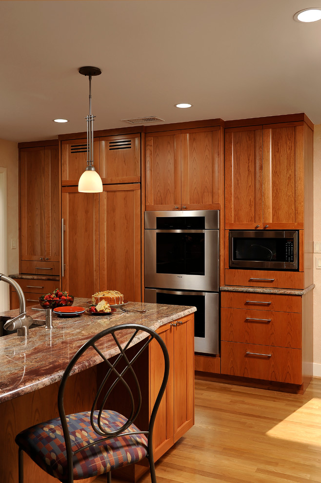Design ideas for a mid-sized transitional l-shaped eat-in kitchen in DC Metro with an undermount sink, flat-panel cabinets, light wood cabinets, granite benchtops, brown splashback, stainless steel appliances, light hardwood floors, with island, glass sheet splashback and beige floor.