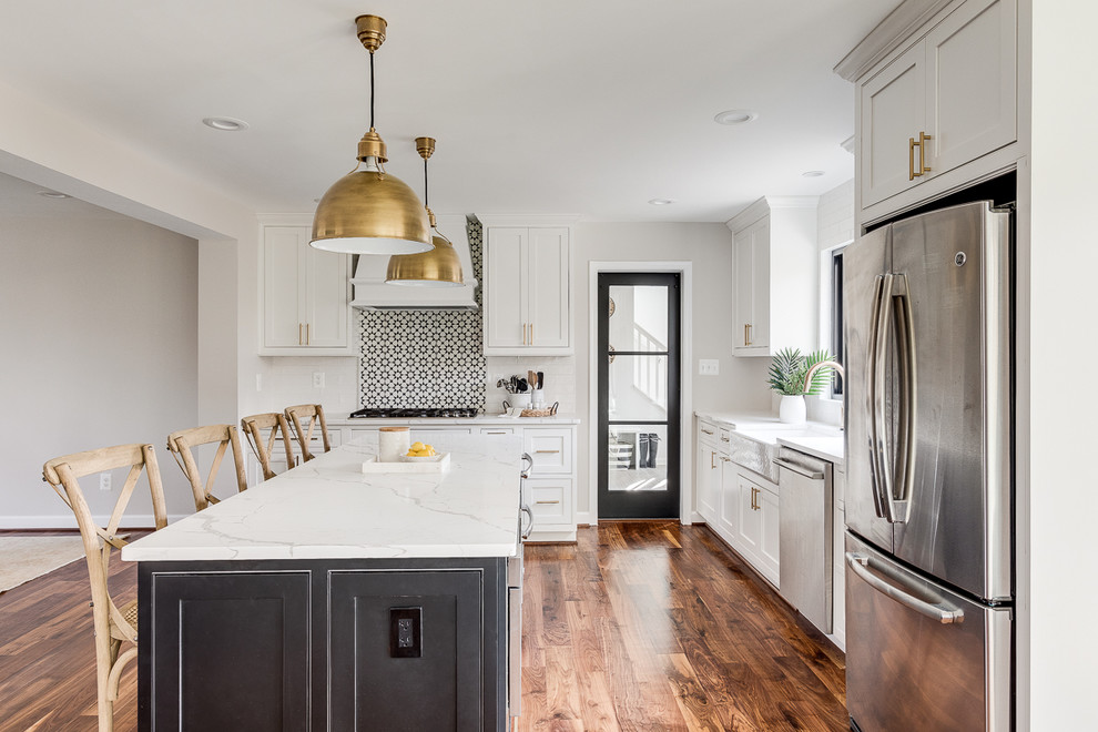 Inspiration for a transitional l-shaped kitchen in DC Metro with a farmhouse sink, shaker cabinets, white cabinets, multi-coloured splashback, stainless steel appliances, medium hardwood floors, with island, brown floor and white benchtop.