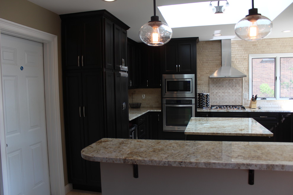 Example of a mid-sized transitional u-shaped beige floor eat-in kitchen design in Cincinnati with recessed-panel cabinets, dark wood cabinets, quartz countertops, beige backsplash, travertine backsplash, stainless steel appliances and an island