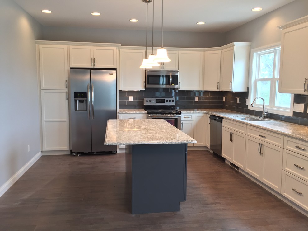 Example of a large transitional l-shaped open concept kitchen design with an undermount sink, raised-panel cabinets, white cabinets, quartz countertops, gray backsplash, stainless steel appliances and an island