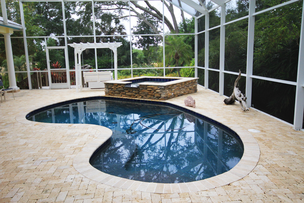 Mid-sized eclectic backyard kidney-shaped natural pool in Tampa with natural stone pavers and a hot tub.
