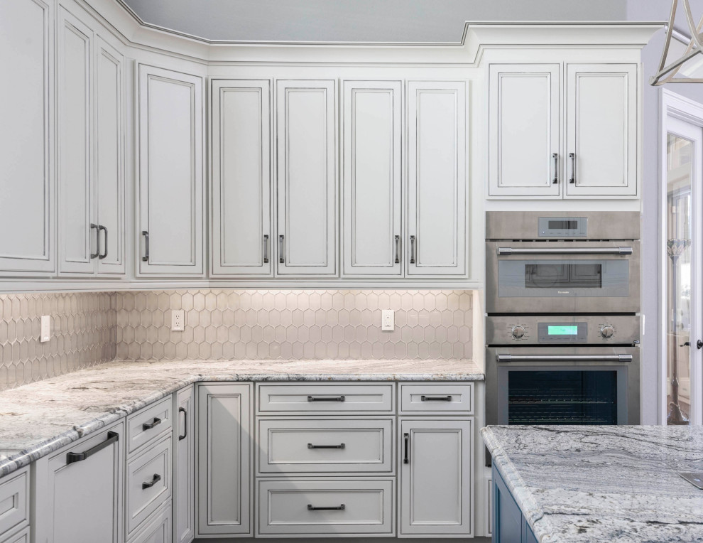 Inspiration for a large transitional u-shaped laminate floor and multicolored floor kitchen remodel in Orlando with an undermount sink, recessed-panel cabinets, white cabinets, granite countertops, metallic backsplash, glass tile backsplash, paneled appliances, an island and gray countertops