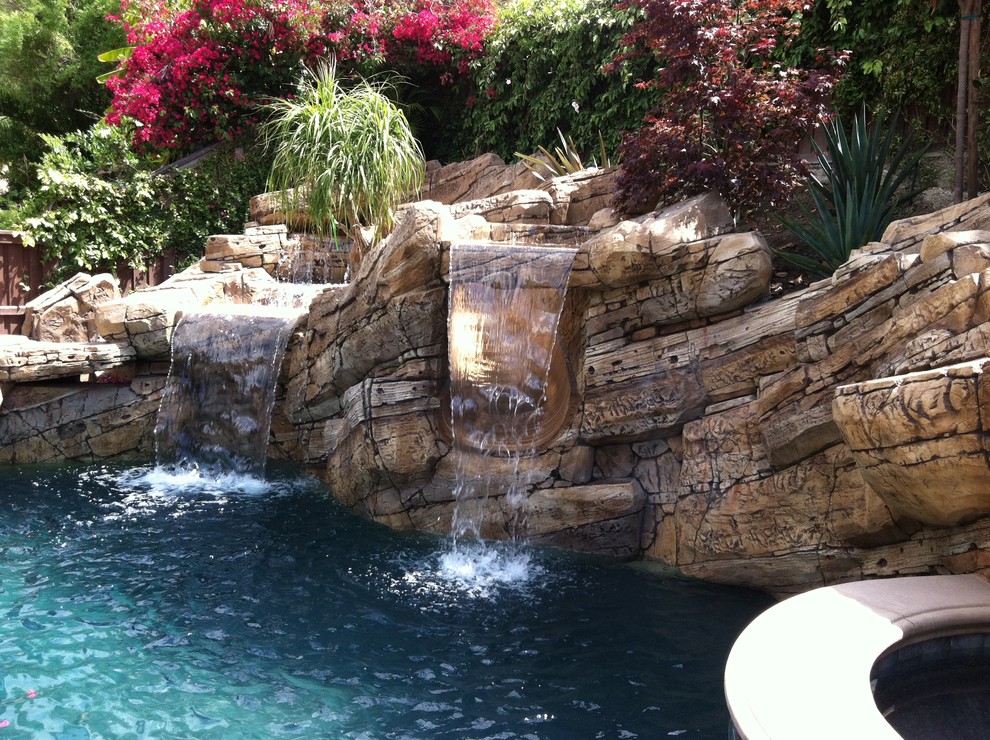 Small tropical backyard natural pool in Orange County with a water feature.
