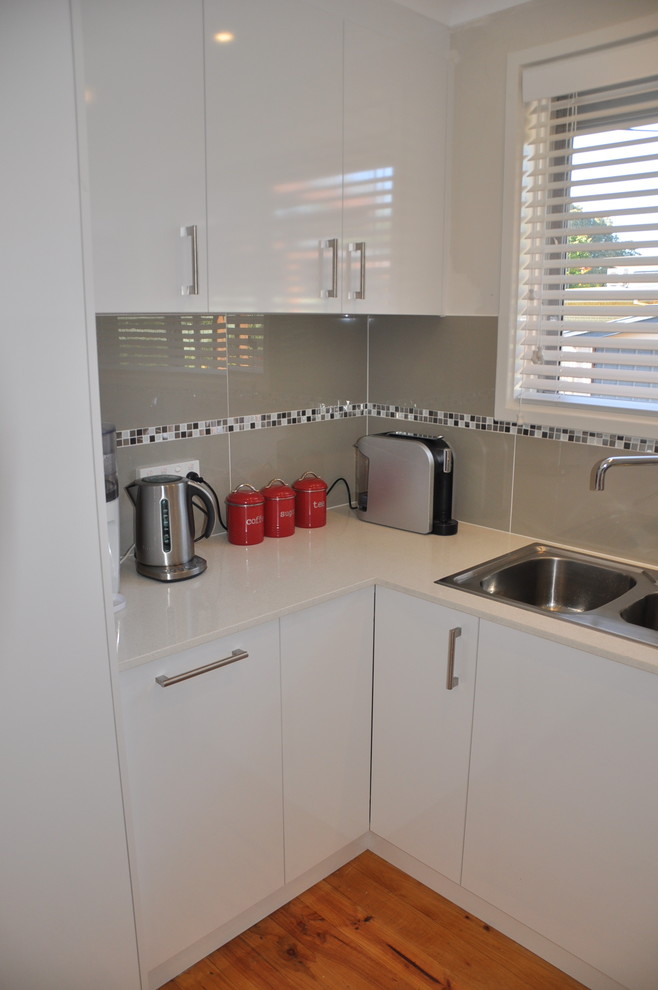 This is an example of a mid-sized modern u-shaped kitchen pantry in Canberra - Queanbeyan with a drop-in sink, white cabinets, quartz benchtops, grey splashback, mosaic tile splashback, stainless steel appliances, light hardwood floors, with island and flat-panel cabinets.