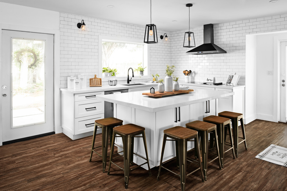 Mid-sized country l-shaped eat-in kitchen in Miami with an undermount sink, shaker cabinets, white cabinets, quartzite benchtops, white splashback, subway tile splashback, black appliances, vinyl floors, with island, brown floor and white benchtop.