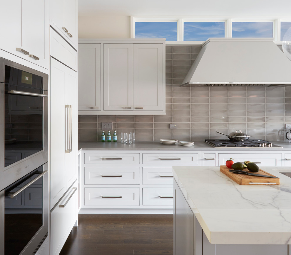 Inspiration for a mid-sized transitional l-shaped eat-in kitchen in Chicago with an undermount sink, shaker cabinets, grey cabinets, onyx benchtops, grey splashback, glass tile splashback, stainless steel appliances, dark hardwood floors and with island.