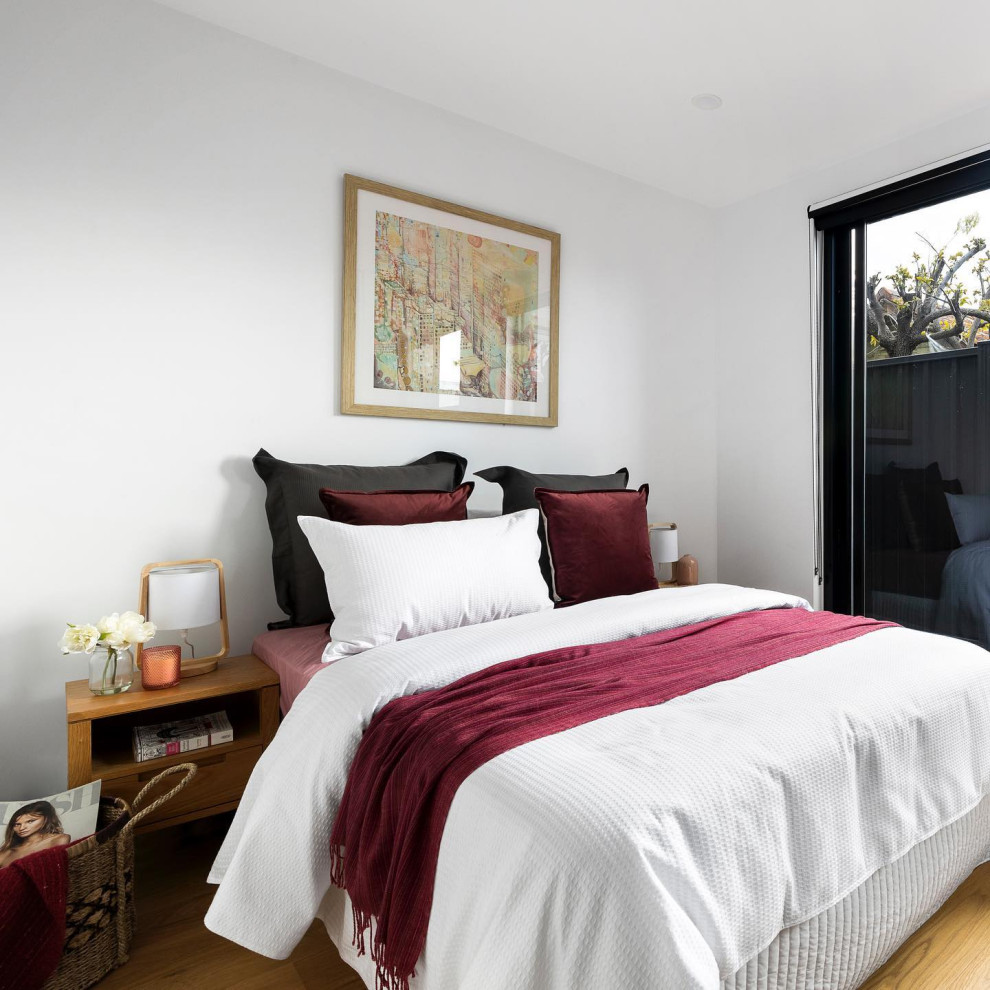 This is an example of a contemporary bedroom in Melbourne with white walls, medium hardwood floors and brown floor.