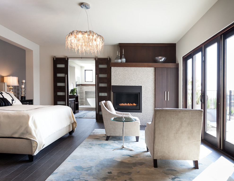 This is an example of a large transitional master bedroom in Sacramento with white walls, porcelain floors, a tile fireplace surround, a corner fireplace and brown floor.