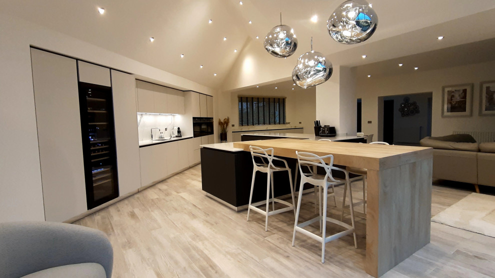 Example of a huge trendy galley vaulted ceiling and porcelain tile open concept kitchen design in Buckinghamshire with flat-panel cabinets, gray cabinets, quartzite countertops, white backsplash, an island, white countertops, a single-bowl sink and black appliances
