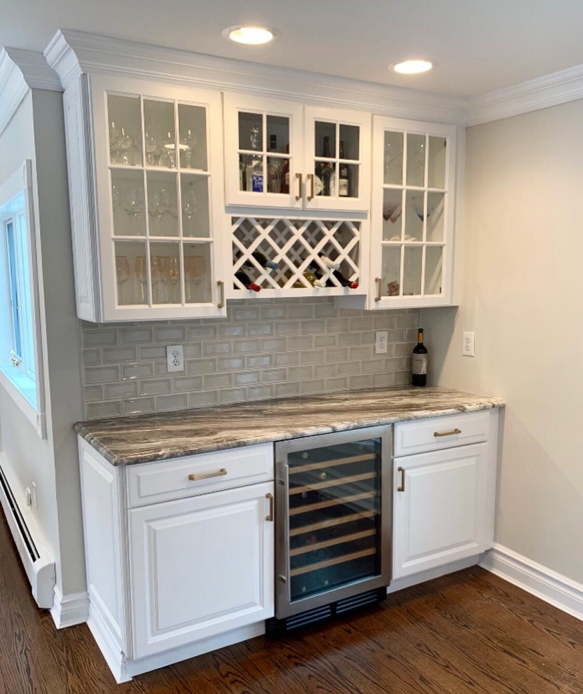 Design ideas for a small transitional single-wall home bar in Other with raised-panel cabinets, white cabinets, granite benchtops, glass tile splashback, medium hardwood floors, brown floor and grey benchtop.