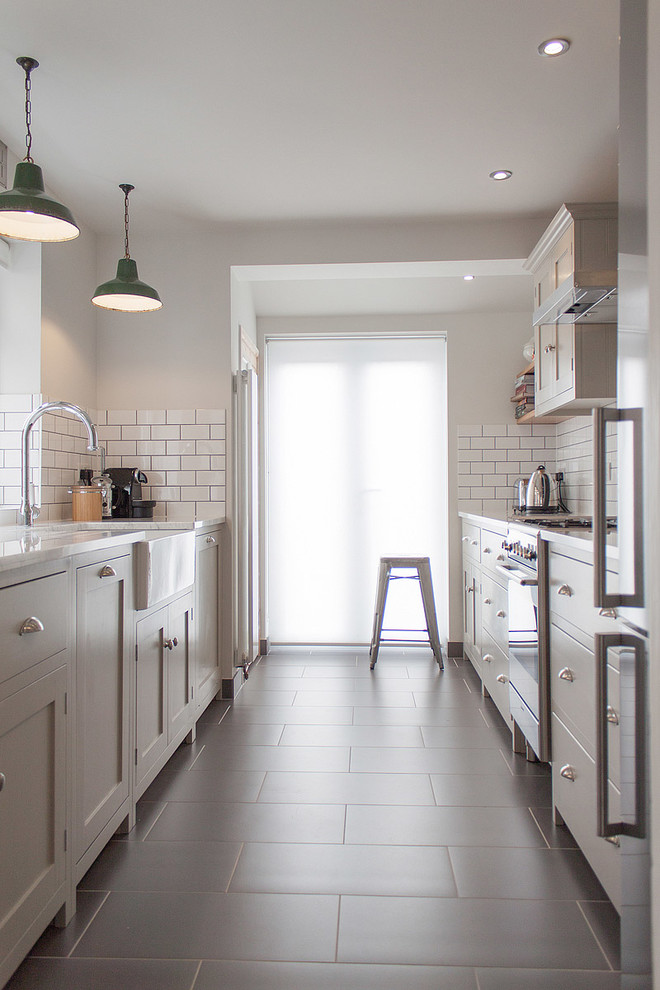 This is an example of a mid-sized contemporary galley separate kitchen in London with a farmhouse sink, shaker cabinets, white splashback and subway tile splashback.