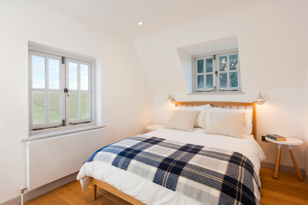 This is an example of a large country guest bedroom in Kent with white walls and medium hardwood floors.