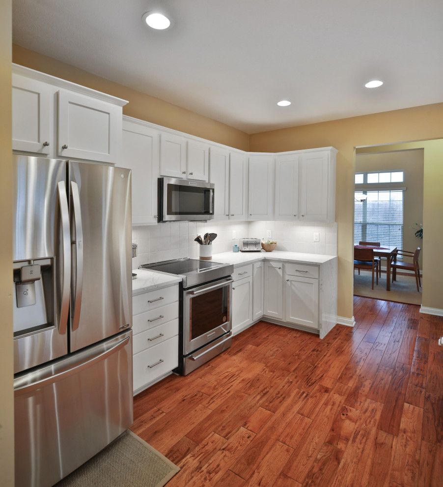 Example of a mid-sized transitional galley medium tone wood floor and brown floor enclosed kitchen design in Columbus with a single-bowl sink, shaker cabinets, white cabinets, quartz countertops, white backsplash, ceramic backsplash, stainless steel appliances, no island and white countertops