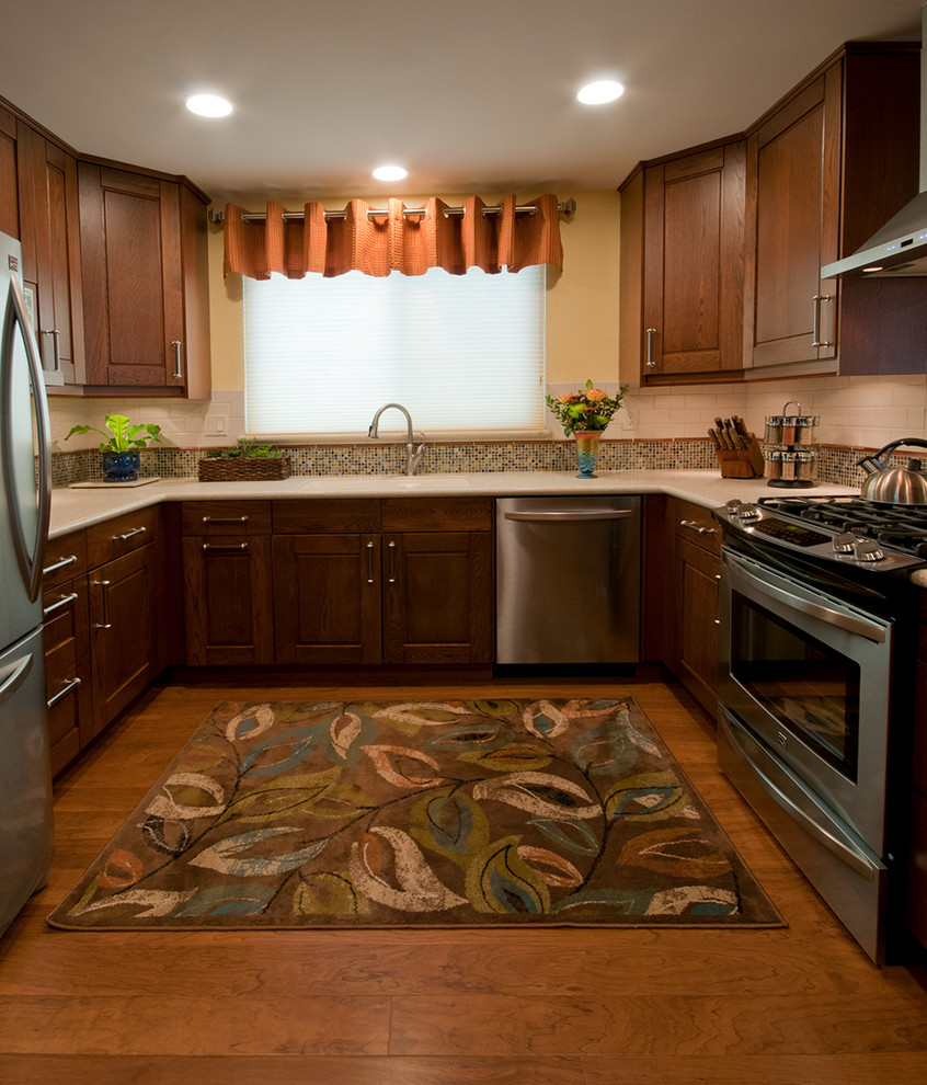 Eat-in kitchen - mid-sized transitional u-shaped medium tone wood floor eat-in kitchen idea in San Diego with an integrated sink, raised-panel cabinets, medium tone wood cabinets, solid surface countertops, stainless steel appliances, multicolored backsplash, mosaic tile backsplash and a peninsula