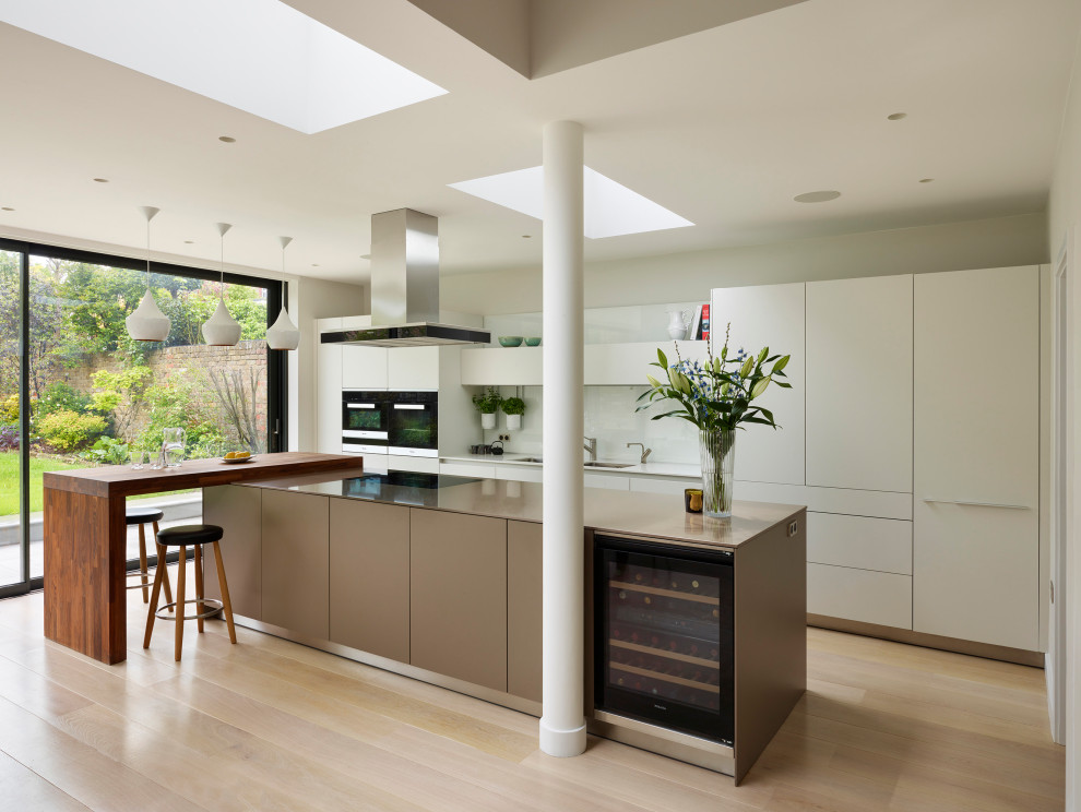 Contemporary single-wall open plan kitchen in Other with a built-in sink, flat-panel cabinets, beige cabinets, engineered stone countertops, beige splashback, engineered quartz splashback, black appliances, light hardwood flooring, an island, beige floors and beige worktops.