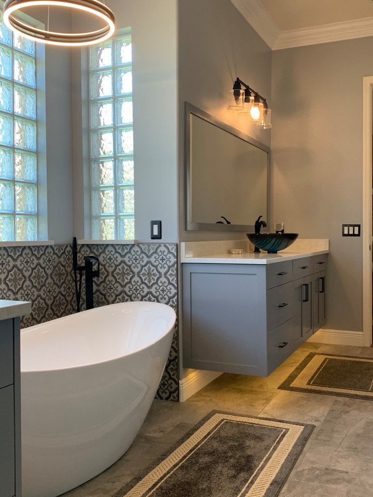 На фото: большая главная ванная комната в современном стиле с фасадами в стиле шейкер, серыми фасадами, отдельно стоящей ванной, душем без бортиков, унитазом-моноблоком, разноцветной плиткой, керамогранитной плиткой, серыми стенами, полом из керамогранита, настольной раковиной, столешницей из искусственного кварца, серым полом, открытым душем, белой столешницей, нишей, тумбой под две раковины, подвесной тумбой и панелями на стенах