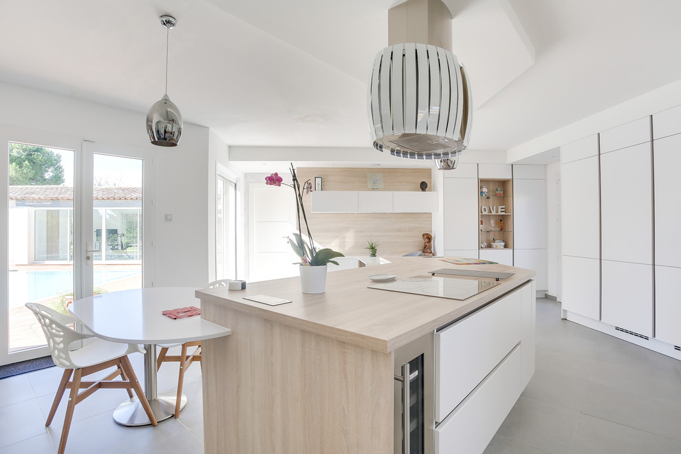 This is an example of a large contemporary galley open plan kitchen in Marseille with a drop-in sink, flat-panel cabinets, white cabinets, wood benchtops, beige splashback, timber splashback, black appliances, with island, grey floor and beige benchtop.