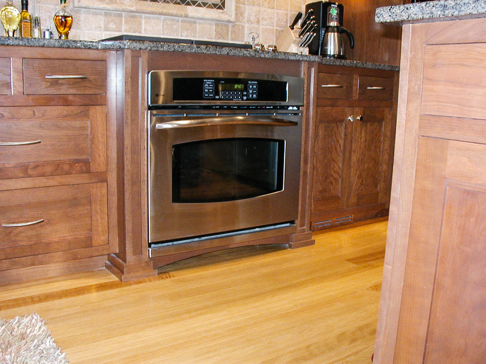 Mid-sized l-shaped eat-in kitchen photo with an undermount sink, shaker cabinets, dark wood cabinets, granite countertops, stainless steel appliances and an island