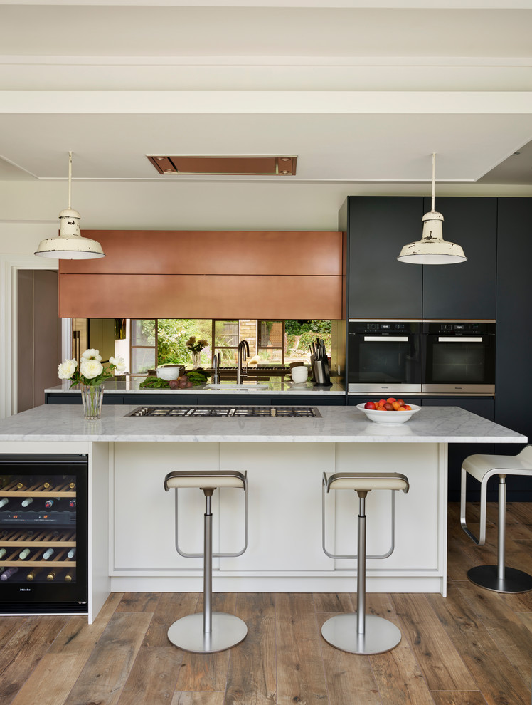 Photo of a large contemporary l-shaped eat-in kitchen in London with an integrated sink, blue cabinets, marble benchtops, metallic splashback, mirror splashback, light hardwood floors, with island, brown floor and white benchtop.