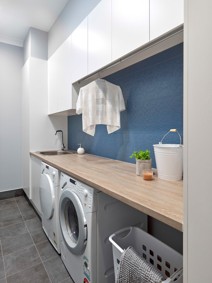 Photo of a small contemporary single-wall dedicated laundry room in Other with a drop-in sink, flat-panel cabinets, white cabinets, laminate benchtops, blue walls, porcelain floors, a side-by-side washer and dryer, grey floor and orange benchtop.
