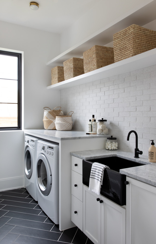 Photo of a modern laundry room in Austin with shaker cabinets, white cabinets, marble benchtops, brick splashback, white walls, porcelain floors and black floor.