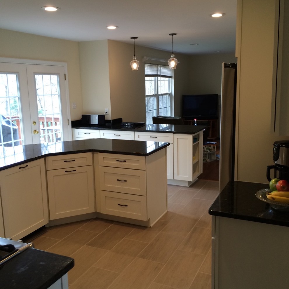 Photo of a mid-sized transitional u-shaped separate kitchen in Baltimore with a farmhouse sink, shaker cabinets, white cabinets, granite benchtops, beige splashback, stone tile splashback, stainless steel appliances, porcelain floors and a peninsula.