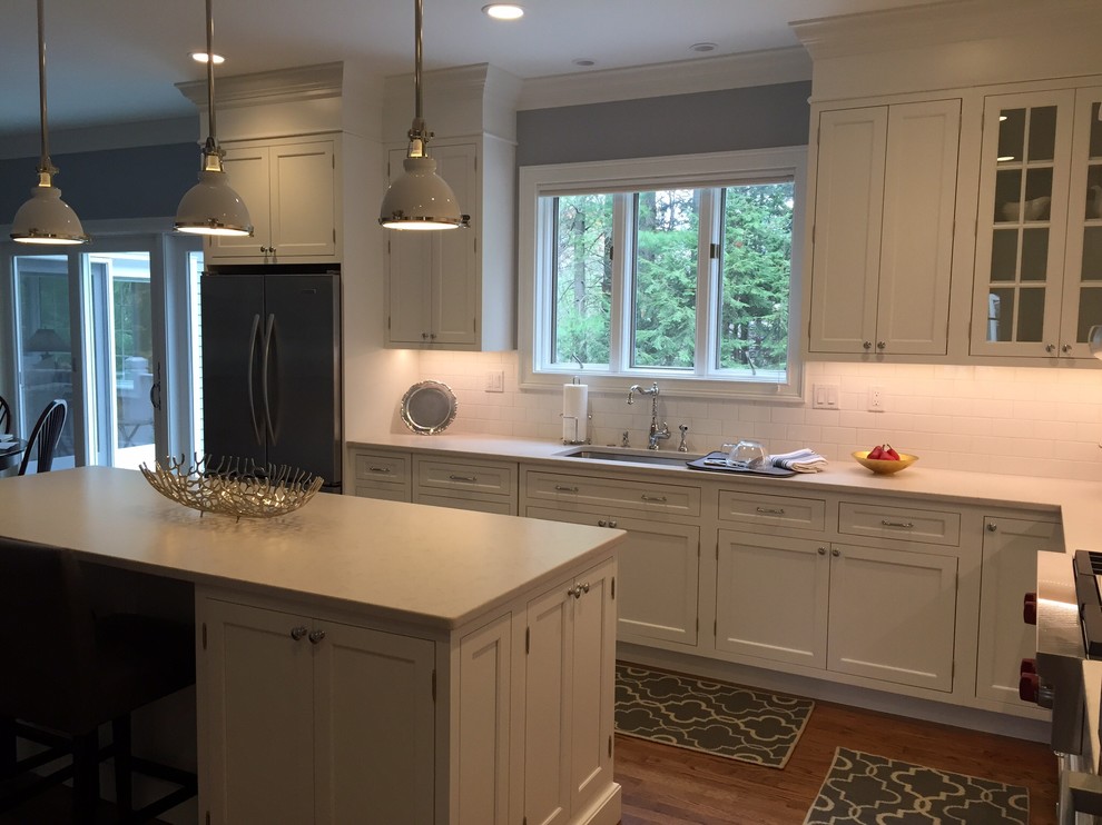 Example of a mid-sized transitional l-shaped medium tone wood floor eat-in kitchen design in Bridgeport with an undermount sink, shaker cabinets, white cabinets, solid surface countertops, white backsplash, subway tile backsplash, stainless steel appliances and an island