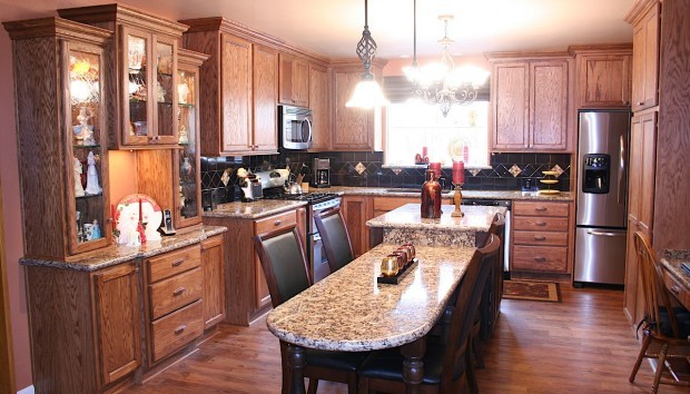 Large elegant u-shaped vinyl floor kitchen photo with an undermount sink, recessed-panel cabinets, medium tone wood cabinets, granite countertops, black backsplash, ceramic backsplash, stainless steel appliances and an island