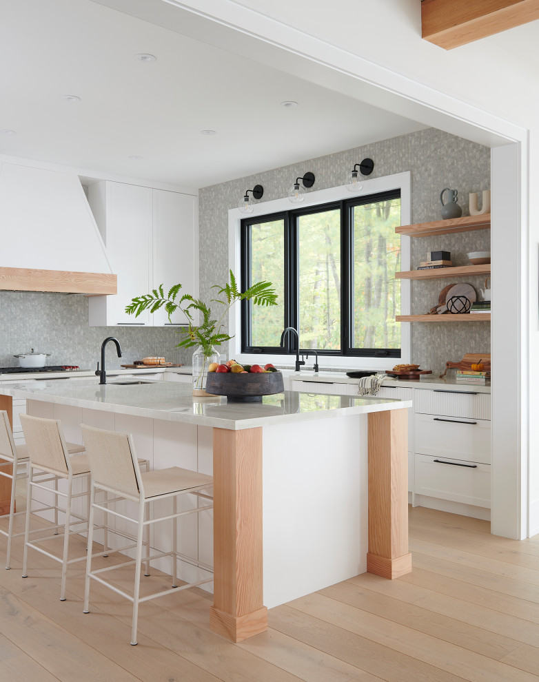 Inspiration for a mid-sized transitional l-shaped open plan kitchen in Toronto with a farmhouse sink, shaker cabinets, white cabinets, quartz benchtops, grey splashback, mosaic tile splashback, light hardwood floors, with island, beige benchtop and beige floor.