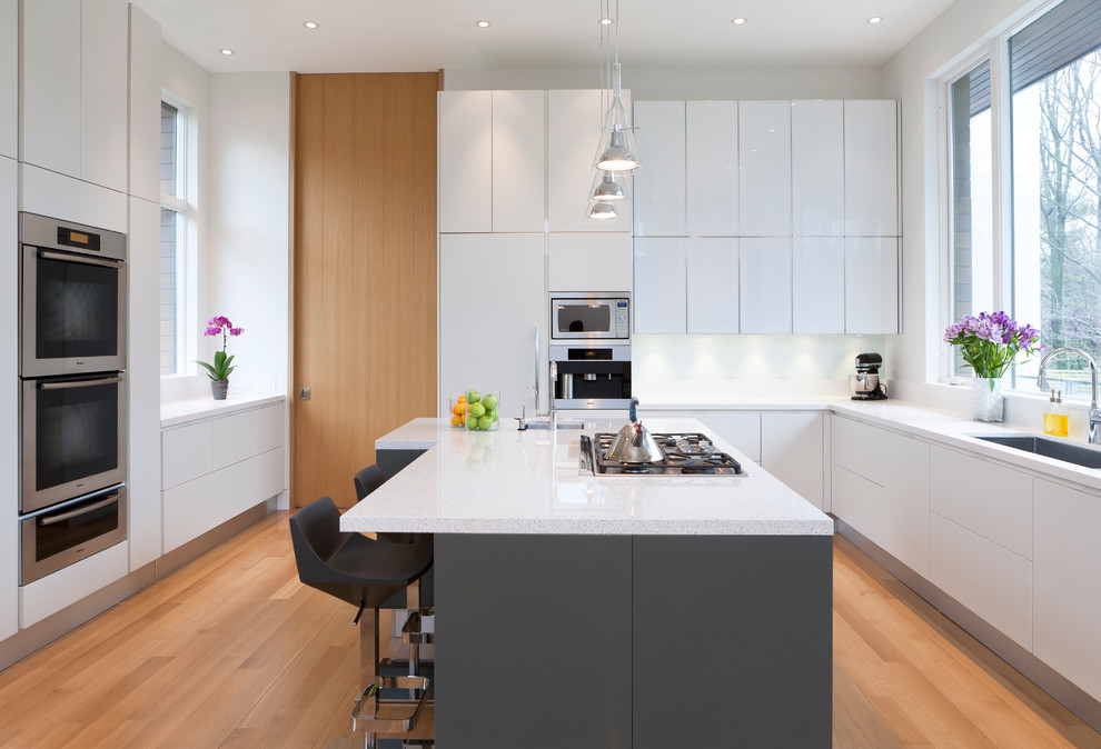 Inspiration for a large contemporary u-shaped separate kitchen in Toronto with an undermount sink, flat-panel cabinets, white cabinets, glass sheet splashback, panelled appliances, white splashback, light hardwood floors, with island, quartz benchtops, brown floor and white benchtop.