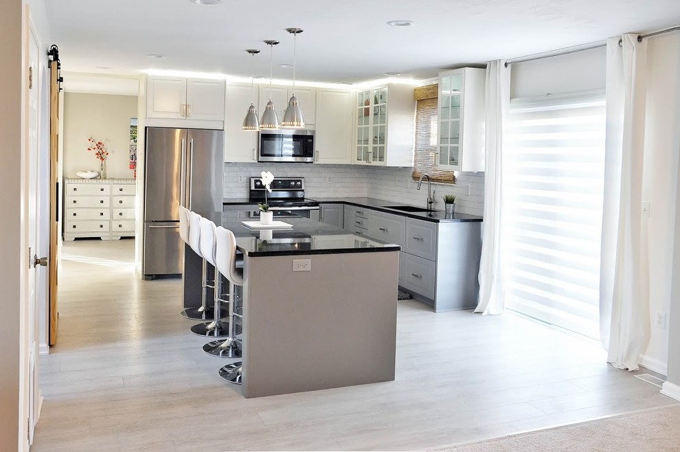 Photo of a small modern l-shaped eat-in kitchen in San Francisco with a drop-in sink, white splashback, with island, shaker cabinets, grey cabinets, quartz benchtops, subway tile splashback, stainless steel appliances, light hardwood floors, beige floor and black benchtop.