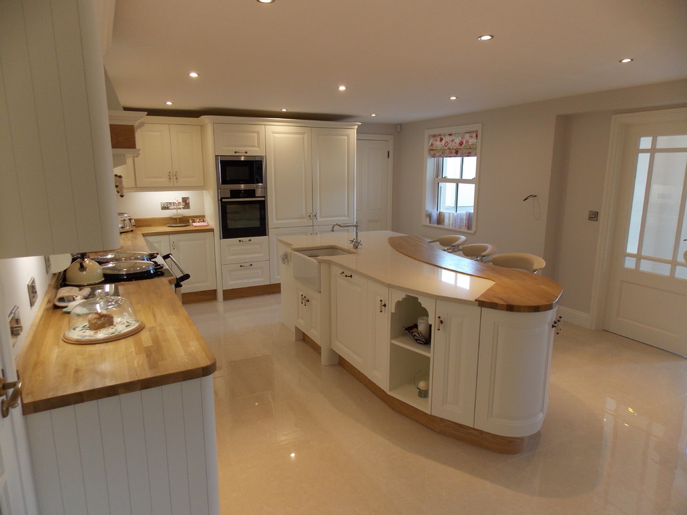 Photo of a mid-sized traditional open plan kitchen in Dublin with a farmhouse sink, raised-panel cabinets, white cabinets, wood benchtops, ceramic splashback, porcelain floors and with island.