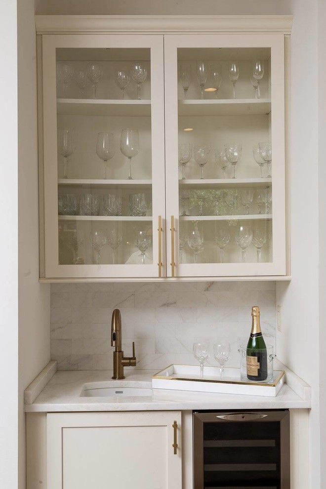 This is an example of a small contemporary single-wall wet bar in New Orleans with an undermount sink, glass-front cabinets, white cabinets, marble benchtops, grey splashback and marble splashback.