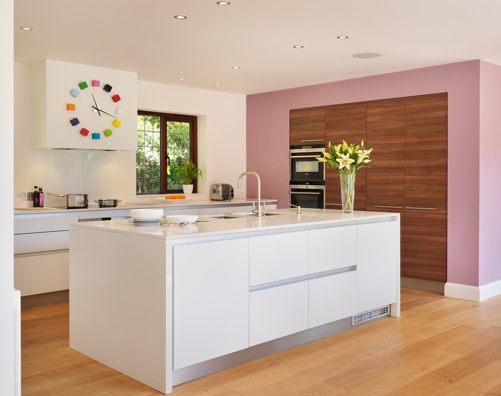This is an example of a contemporary l-shaped open plan kitchen in Venice with an undermount sink, flat-panel cabinets, white cabinets, white splashback, stainless steel appliances, light hardwood floors and with island.