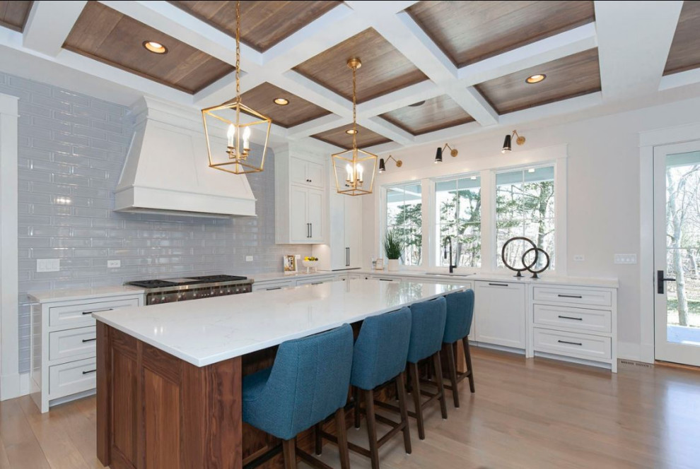 Large country u-shaped kitchen in Chicago with an undermount sink, shaker cabinets, white cabinets, quartz benchtops, grey splashback, subway tile splashback, stainless steel appliances, light hardwood floors, with island, brown floor, white benchtop and coffered.
