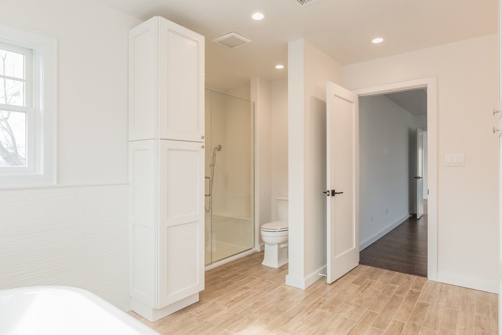 This is an example of a mid-sized contemporary master bathroom in New York with beaded inset cabinets, beige cabinets, a freestanding tub, an alcove shower, a two-piece toilet, white tile, porcelain tile, white walls, porcelain floors, an undermount sink, engineered quartz benchtops, brown floor, a sliding shower screen and beige benchtops.