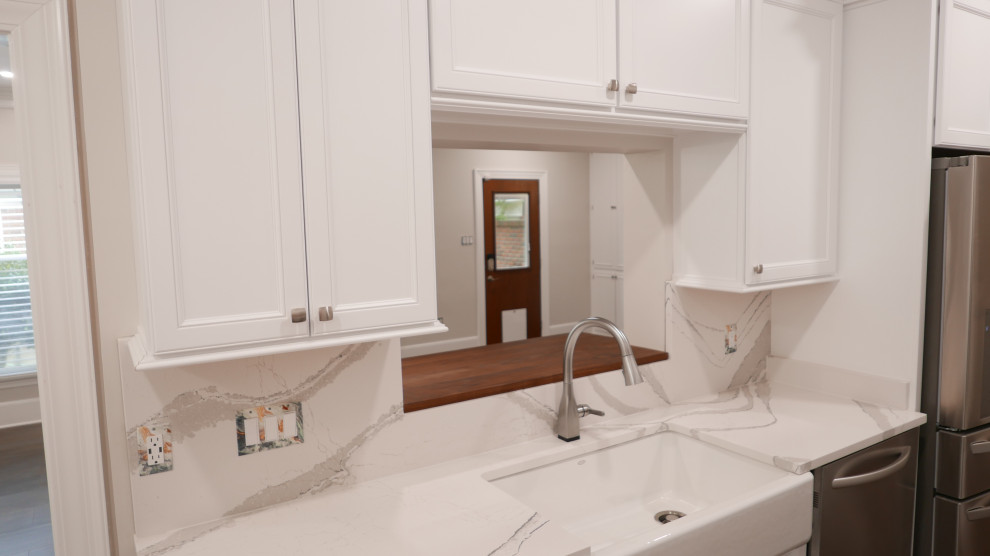 Example of a mid-sized transitional galley laminate floor and multicolored floor eat-in kitchen design with a farmhouse sink, shaker cabinets, white cabinets, quartz countertops, white backsplash, quartz backsplash, stainless steel appliances and white countertops