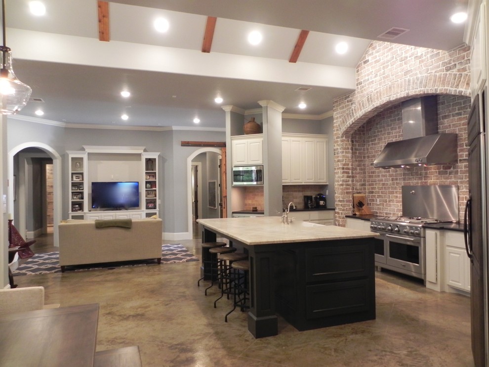 Photo of a large arts and crafts l-shaped eat-in kitchen in Houston with a farmhouse sink, white cabinets, stainless steel appliances, concrete floors, with island, raised-panel cabinets, granite benchtops and red splashback.