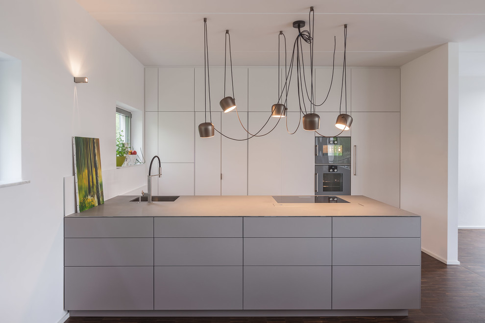 Küche mit integriertem Waschbecken, flächenbündigen Schrankfronten, Edelstahl-Arbeitsplatte und Halbinsel in Leipzig
