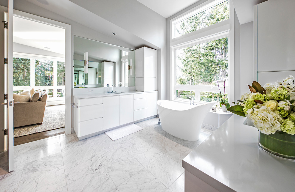 Design ideas for a large contemporary master bathroom in Seattle with flat-panel cabinets, white cabinets, a freestanding tub, white tile, stone tile, marble floors, an undermount sink, engineered quartz benchtops, grey walls, white floor and white benchtops.