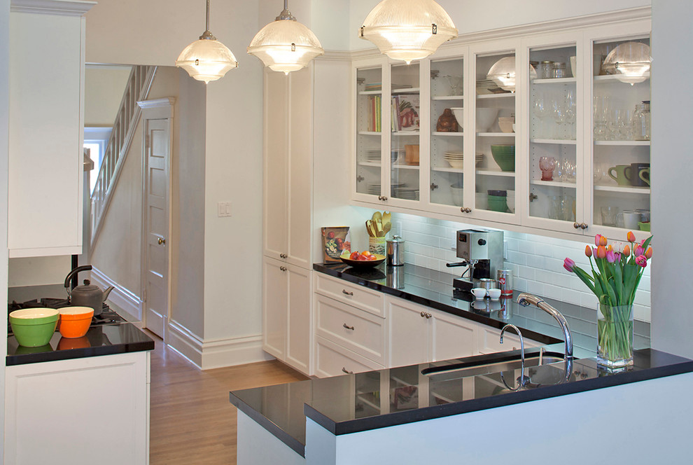 This is an example of a mid-sized traditional u-shaped separate kitchen in San Francisco with an undermount sink, white cabinets, white splashback, subway tile splashback, recessed-panel cabinets, quartz benchtops and light hardwood floors.