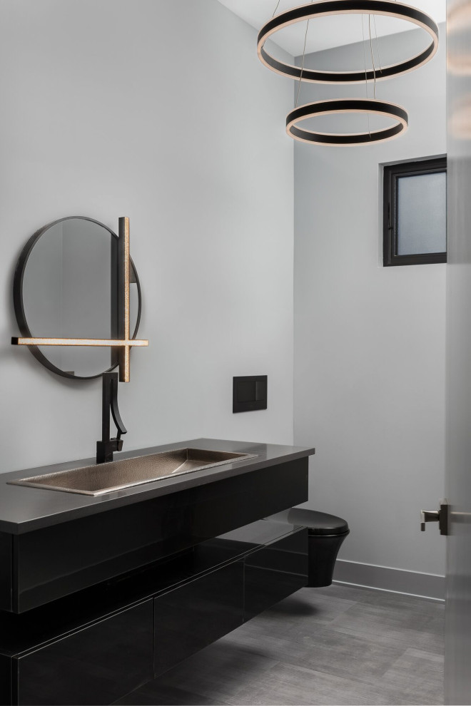 Inspiration for a mid-sized powder room in Chicago with flat-panel cabinets, black cabinets, a wall-mount toilet, gray tile, grey walls, a trough sink, grey floor, grey benchtops and a floating vanity.