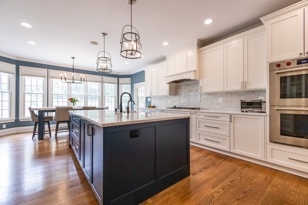 Inspiration for a large transitional u-shaped medium tone wood floor and brown floor eat-in kitchen remodel in Baltimore with a farmhouse sink, shaker cabinets, blue cabinets, quartz countertops, white backsplash, marble backsplash, stainless steel appliances, an island and white countertops