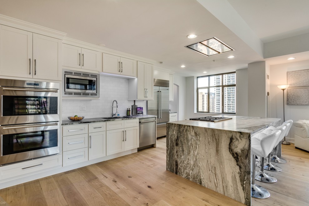 Photo of a large modern galley kitchen in Chicago with beaded inset cabinets, white cabinets, marble benchtops, stainless steel appliances, light hardwood floors, with island, beige floor and multi-coloured benchtop.