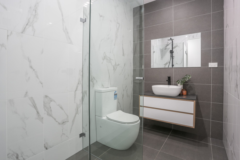 Photo of a medium sized modern ensuite bathroom in Sydney with flat-panel cabinets, light wood cabinets, a corner shower, a bidet, white tiles, porcelain tiles, white walls, ceramic flooring, a vessel sink, engineered stone worktops, grey floors, a hinged door, grey worktops, a wall niche, a single sink, a floating vanity unit, a timber clad ceiling and brick walls.